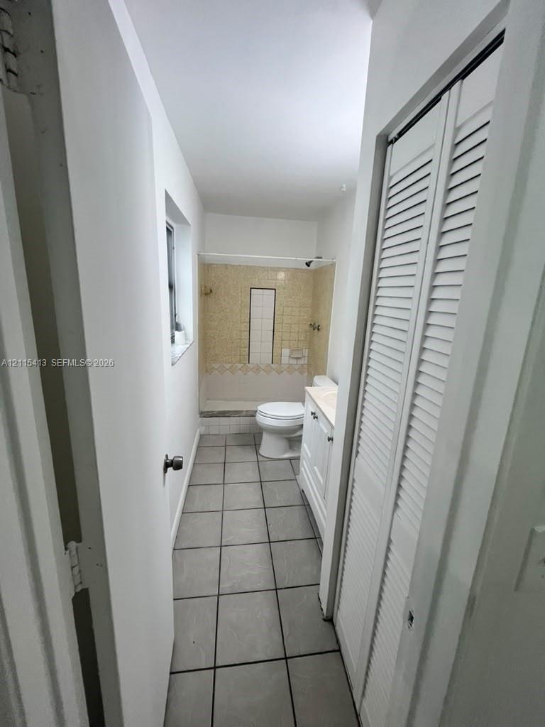 Bathroom featuring a tiled shower enclosure, white vanity cabinet, ceramic tile flooring, and a louvered closet door
