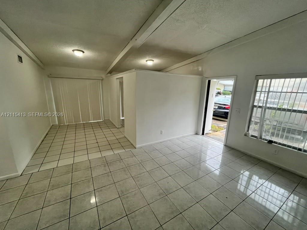 Interior space featuring light-colored ceramic tile flooring, vaulted ceilings with exposed beams, recessed lighting, and vertical window blinds