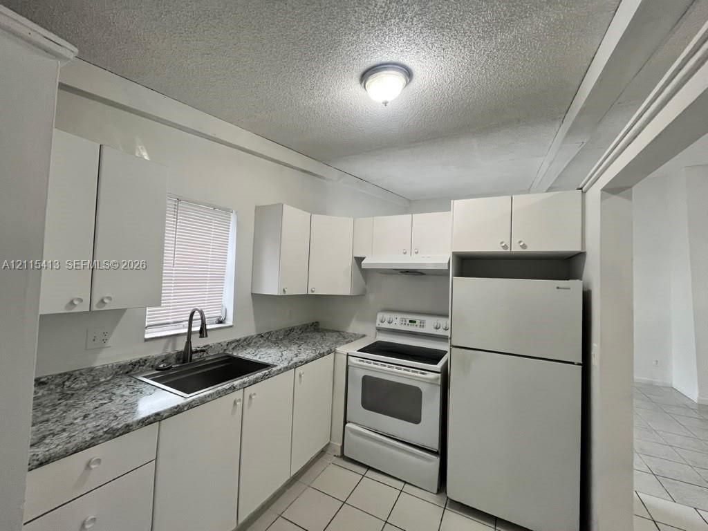 Kitchen featuring white cabinetry, stone-finish countertops, tile flooring, and integrated white appliances
