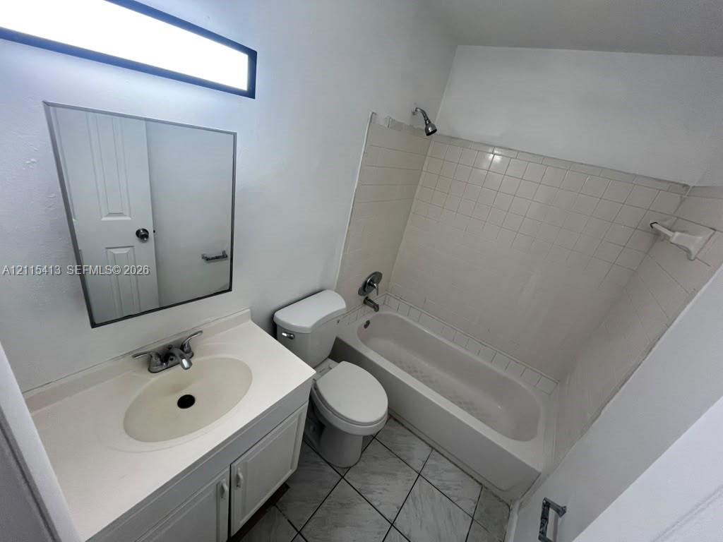 Bathroom featuring a vanity with an integrated sink, rectangular wall-mounted mirror, ceramic tile flooring, and a tub-shower combination with tiled surround