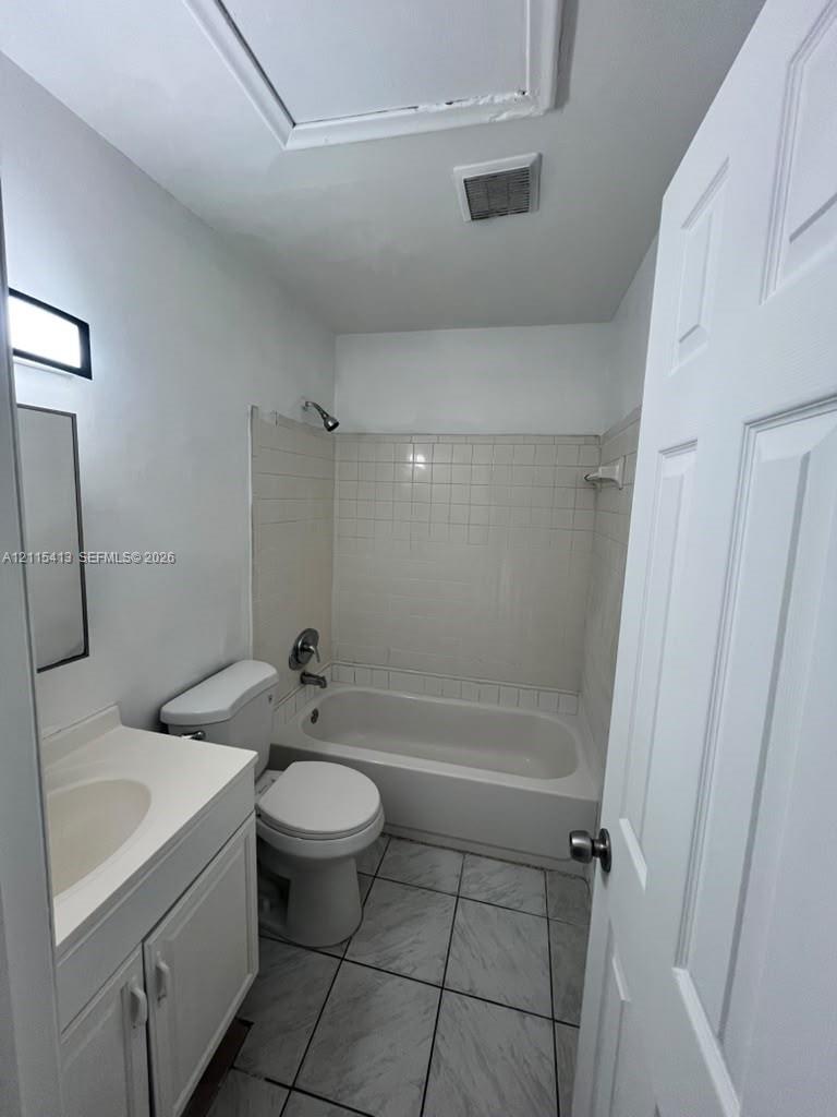 Bathroom featuring a vanity with an integrated sink, porcelain-tiled tub surround, a combination shower and soaking tub, and tile flooring
