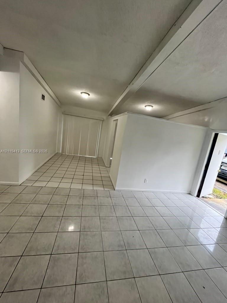 Interior space featuring ceramic tile flooring, neutral wall finishes, exposed structural beams, flush-mount lighting, and vertical blinds