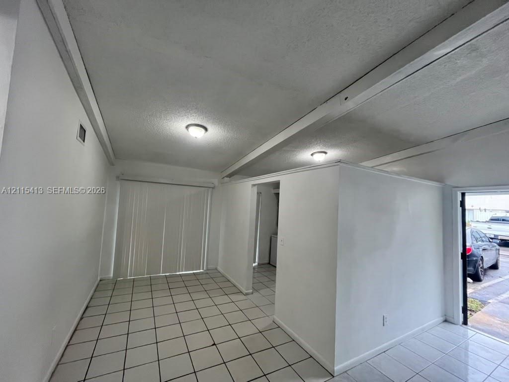 Interior space featuring neutral tile flooring, exposed ceiling beams, flush-mount lighting, and vertical sliding glass doors