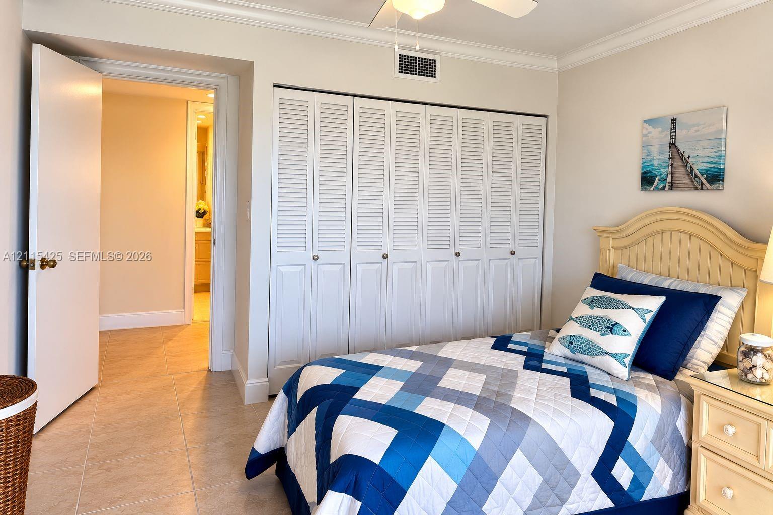 Neutral-tone room featuring tile flooring, crown molding, a ceiling fan, and floor-to-ceiling bi-fold closet doors