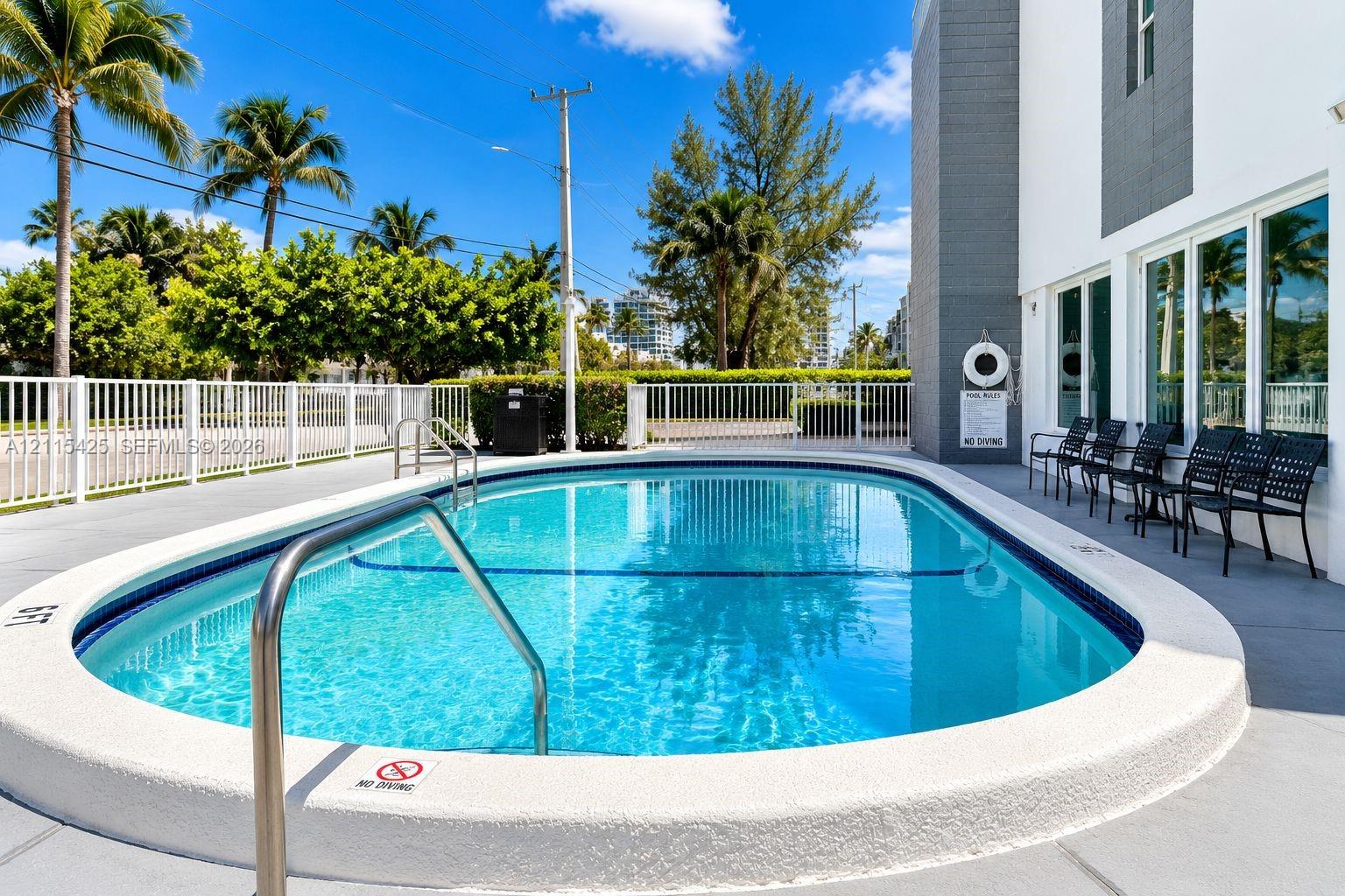 Oval swimming pool featuring a concrete deck, metal safety fencing, and stainless steel handrails