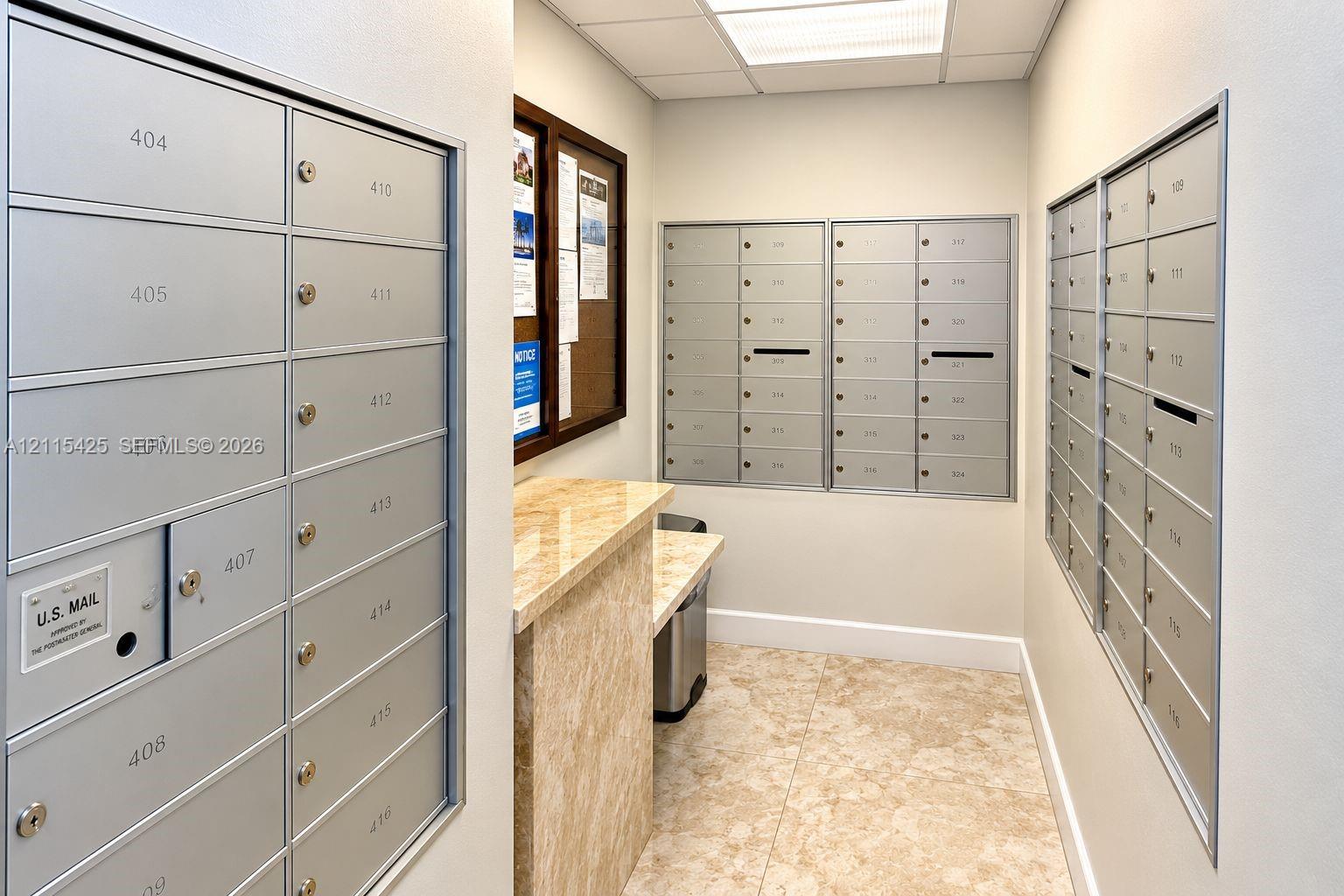 Dedicated mailroom featuring recessed metallic mailboxes, stone-surfaced counter, and stone-tile flooring