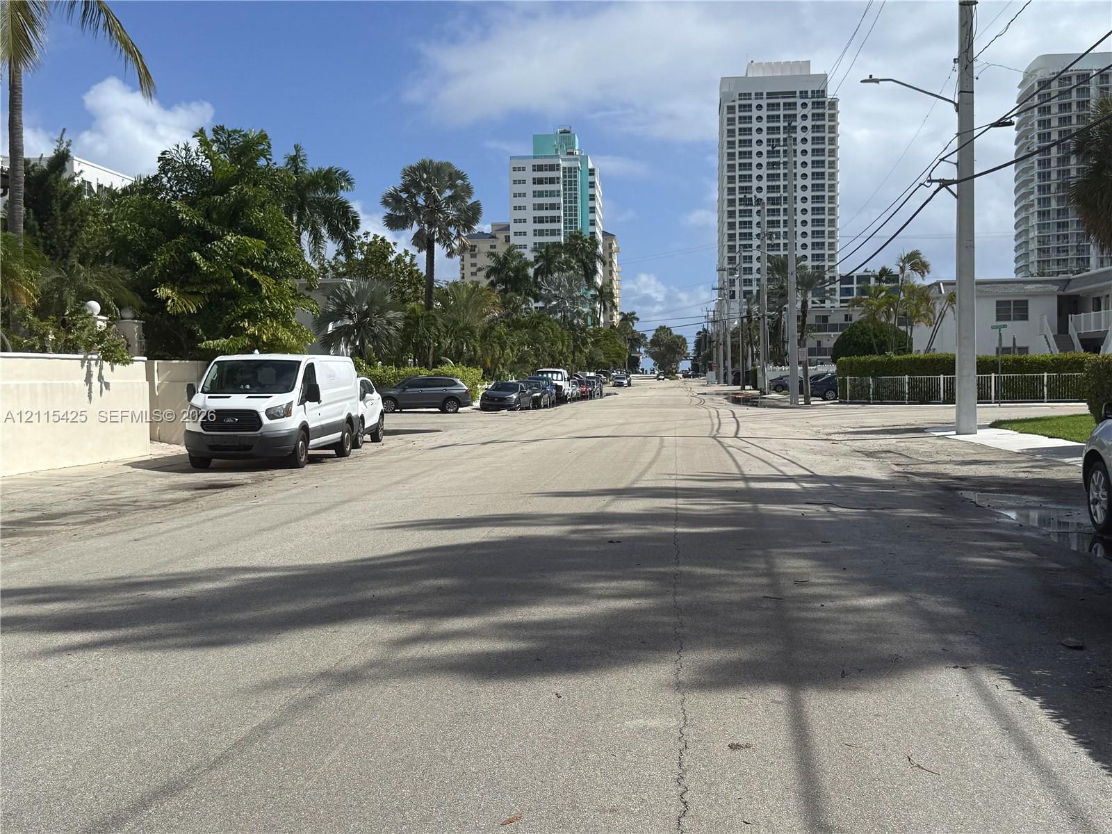 Paved public street bordered by mature palm trees, tropical landscaping, and high-rise structures