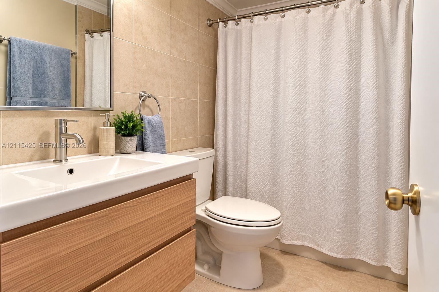 Bathroom featuring a wood-finish floating vanity with a rectangular integrated sink, brushed nickel faucet, large wall-mounted mirror, and neutral-toned wall tiling