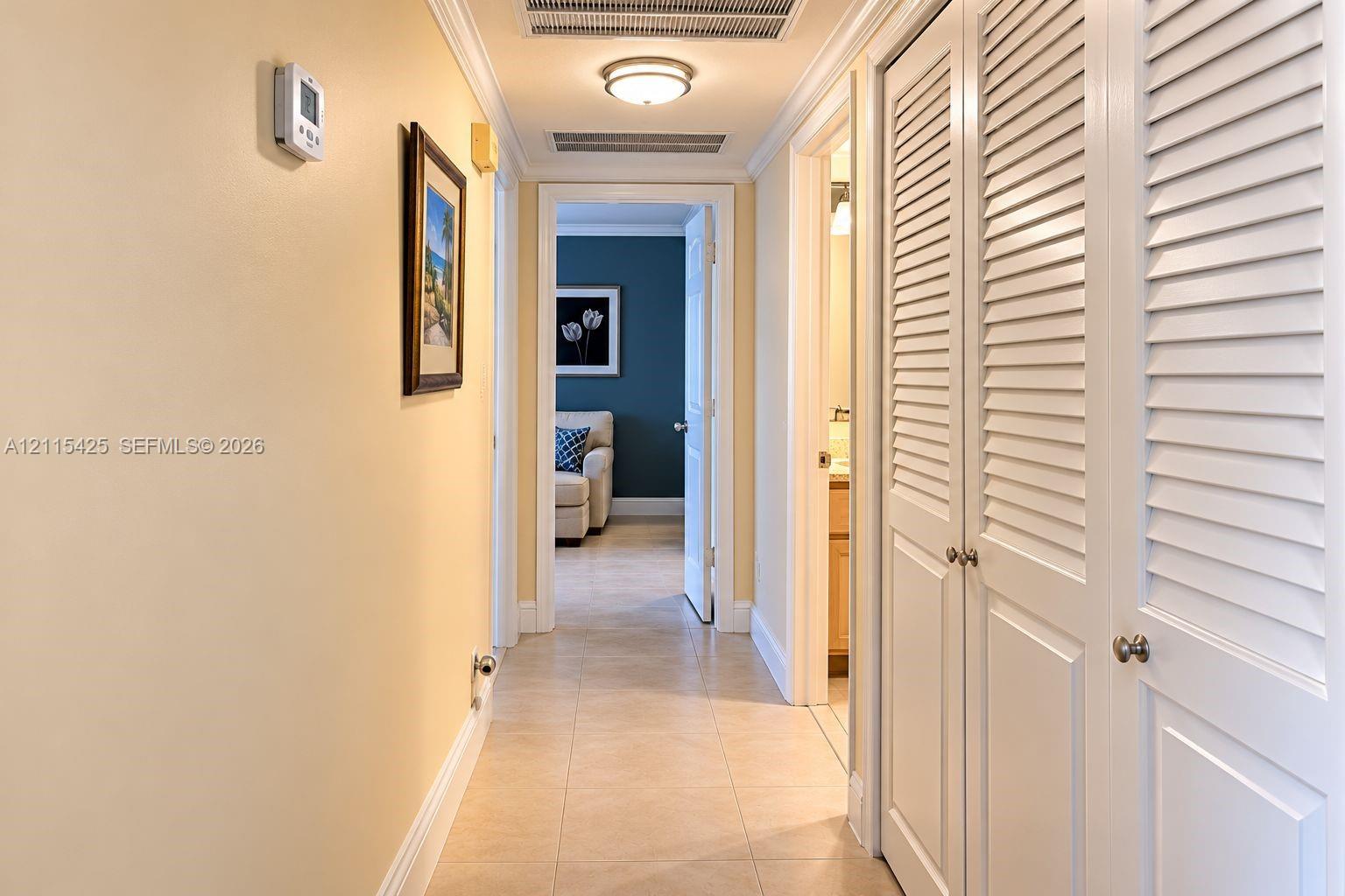 Hallway featuring large-format tile flooring, crown molding, and white louvered-style closet doors