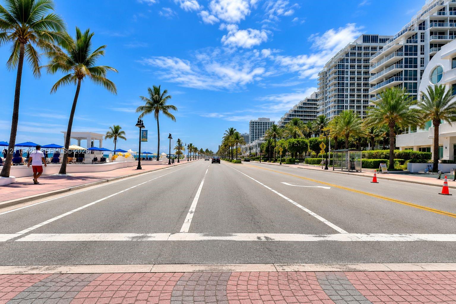 Coastal thoroughfare featuring paved multi-lane roadway, interlocking brick sidewalks, and established palm trees
