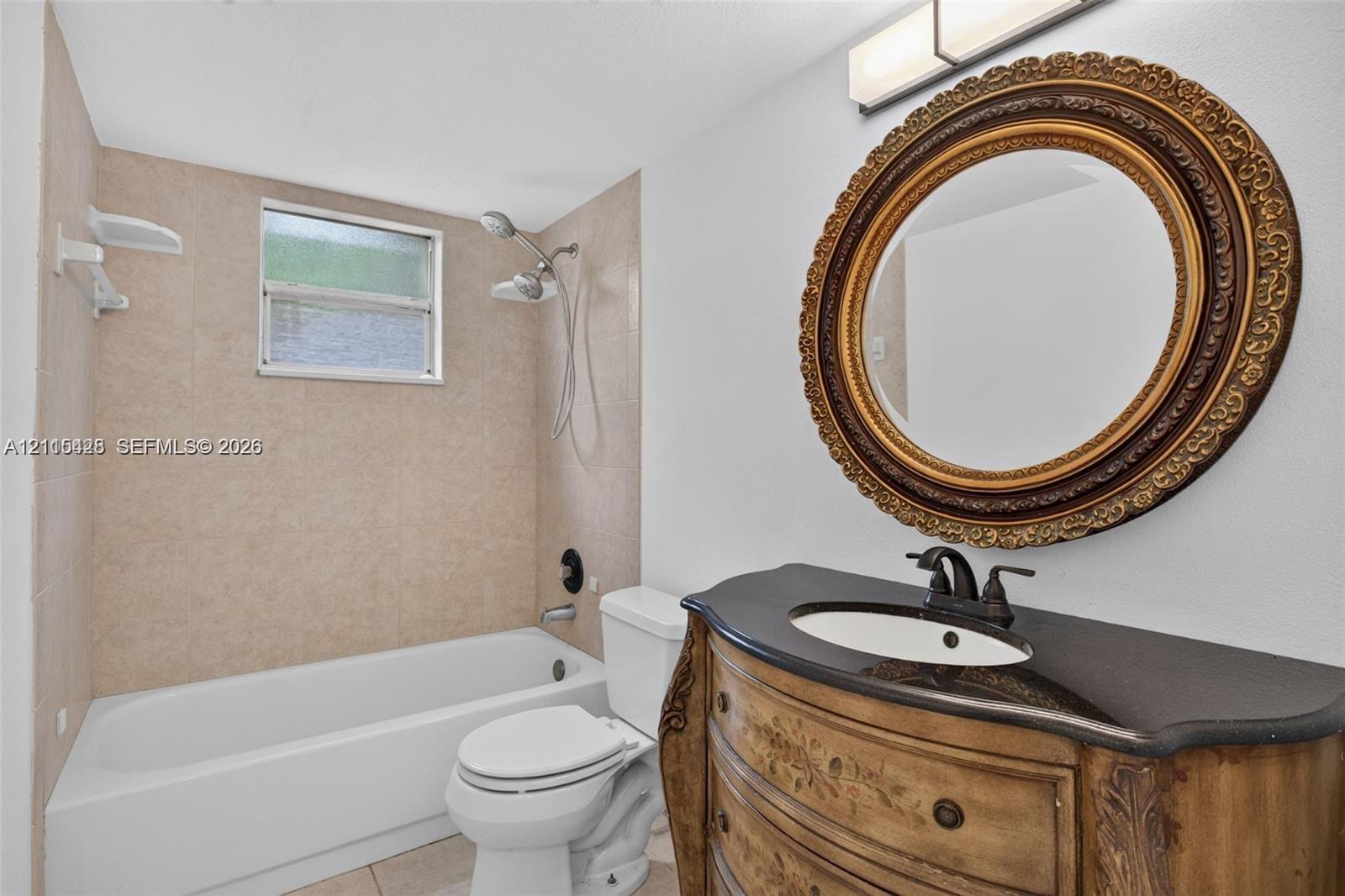 Bathroom featuring a built-in vanity with a stone countertop, an integrated sink with a multi-handle faucet, a shower-tub combination with tile surround, and a wall-mounted light fixture