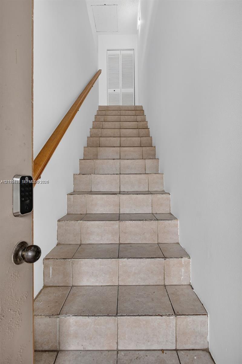 Staircase featuring tile treads, a wood-finish handrail, and white louvered-panel double doors