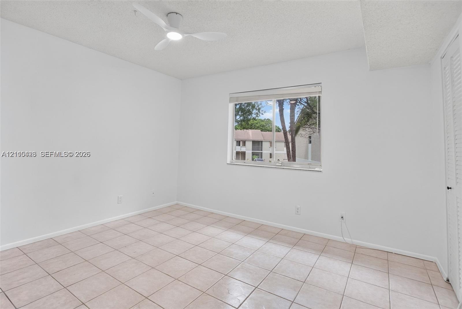 Interior room featuring neutral wall-to-wall ceramic tile flooring, a white ceiling fan with integrated lighting, and a single window with white horizontal blinds