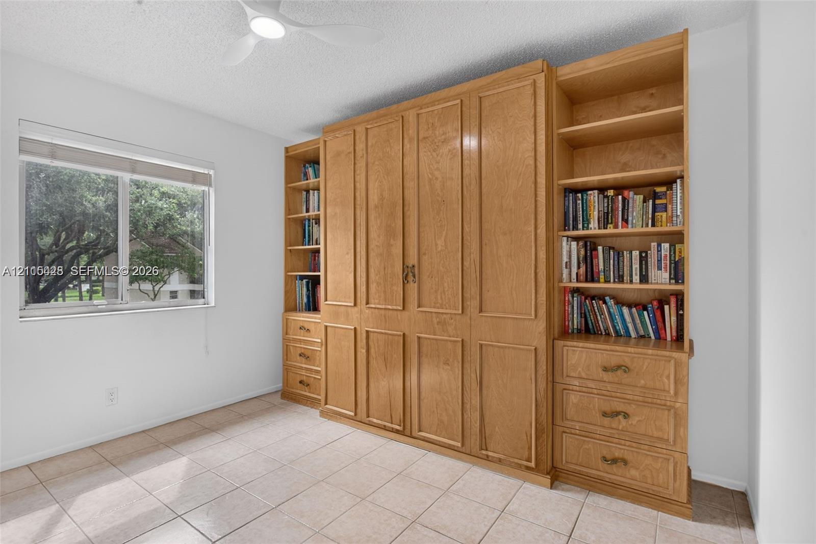 Built-in wood cabinetry featuring recessed panel doors, drawers with metallic hardware, and integrated open shelving, paired with tile flooring and a ceiling-mounted light fixture