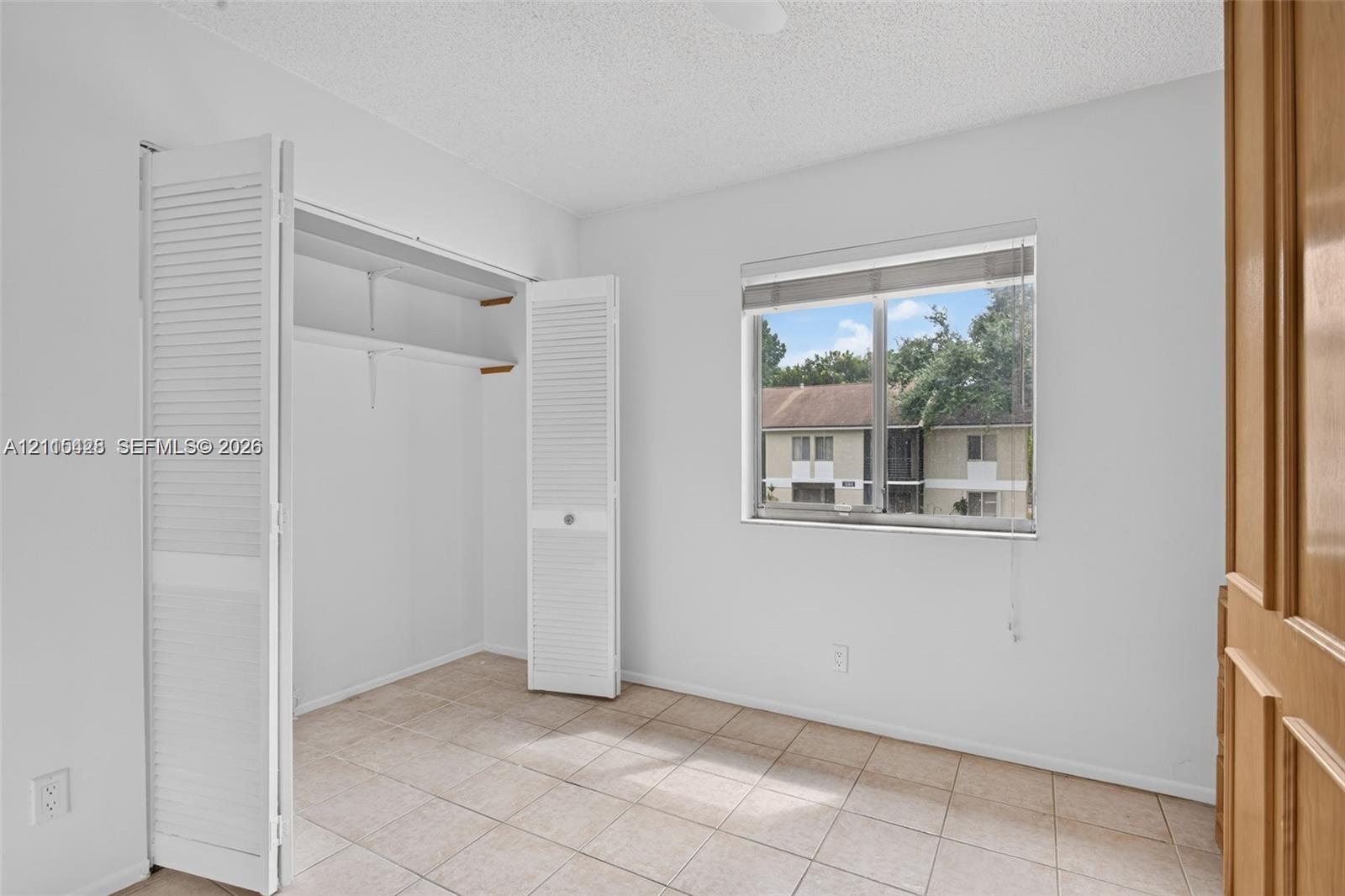 Room featuring tile flooring, a closet with louvered bifold doors, and a window with a roller shade