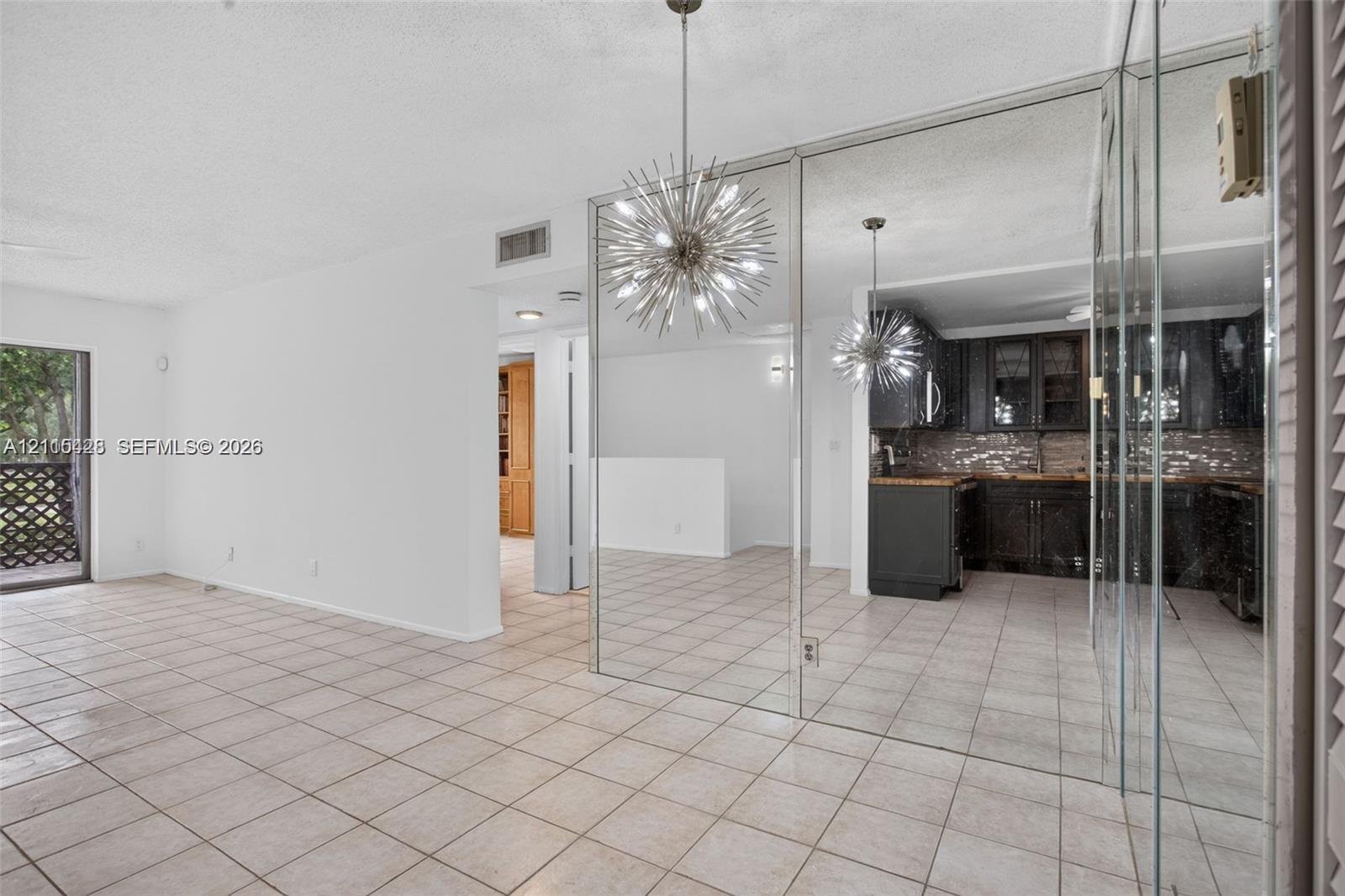Living area featuring tile flooring, floor-to-ceiling wall mirrors, and a multi-arm sputnik-style pendant light fixture