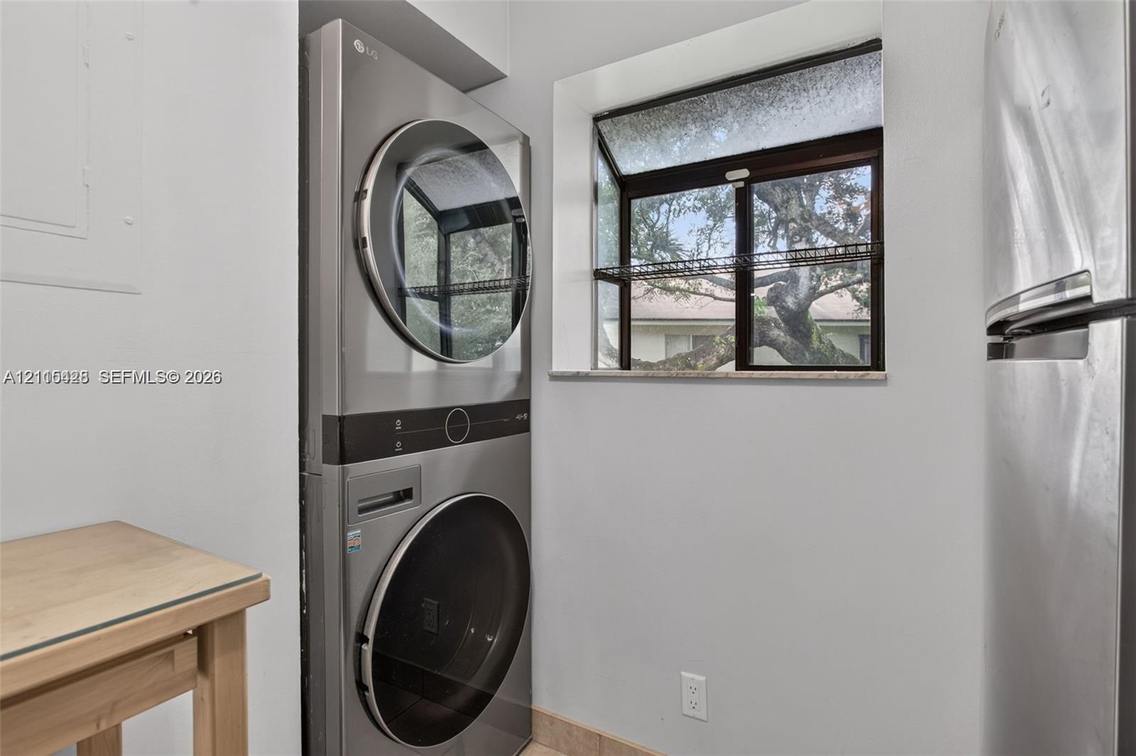 Laundry area featuring a stainless steel stacked washer and dryer, single-pane window with stone-finish sill, and neutral tile flooring
