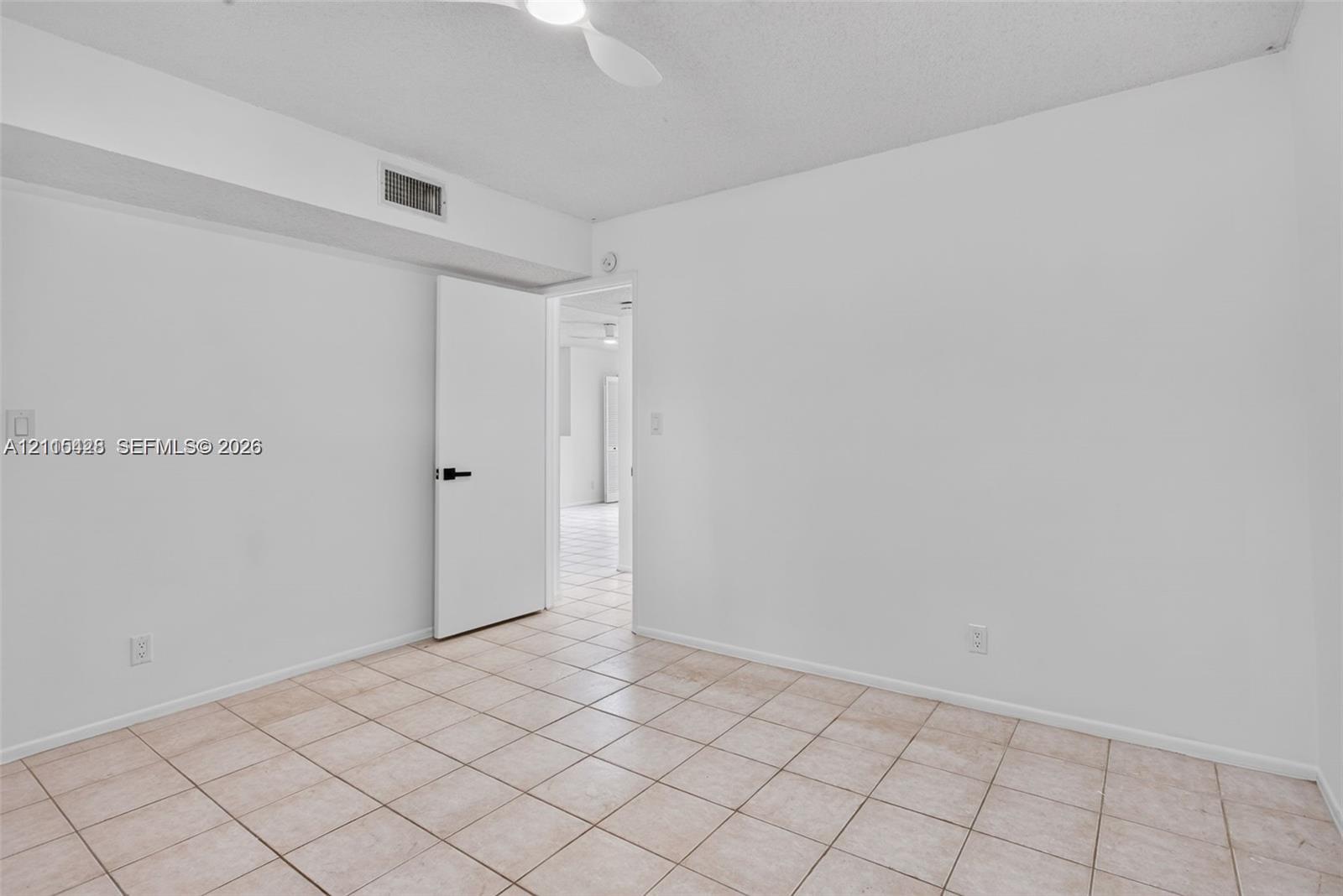 Neutral-toned ceramic tile flooring, solid-core interior door with matte black hardware, and ceiling-mounted fan fixture