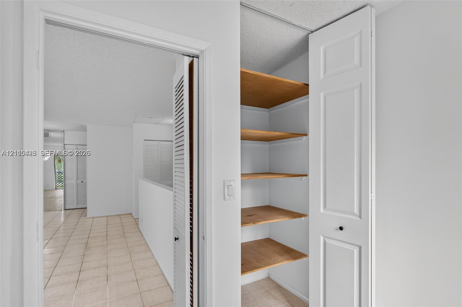 Built-in storage closet featuring multi-level wooden shelving and bi-fold doors, complemented by ceramic tile flooring