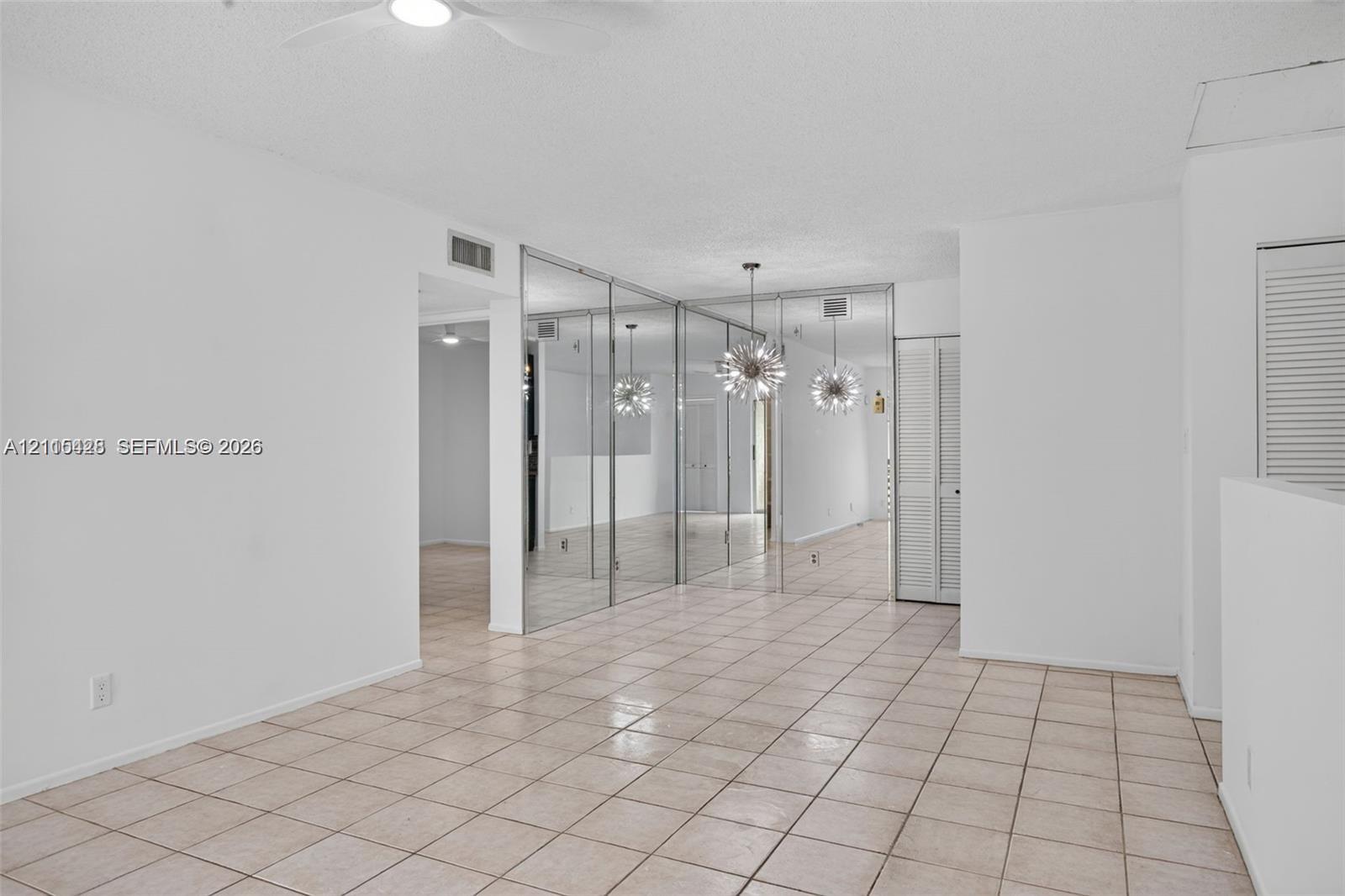 Living area featuring neutral tile flooring, floor-to-ceiling mirrored closet doors, a ceiling fan with light fixture, and louvered bifold closet doors
