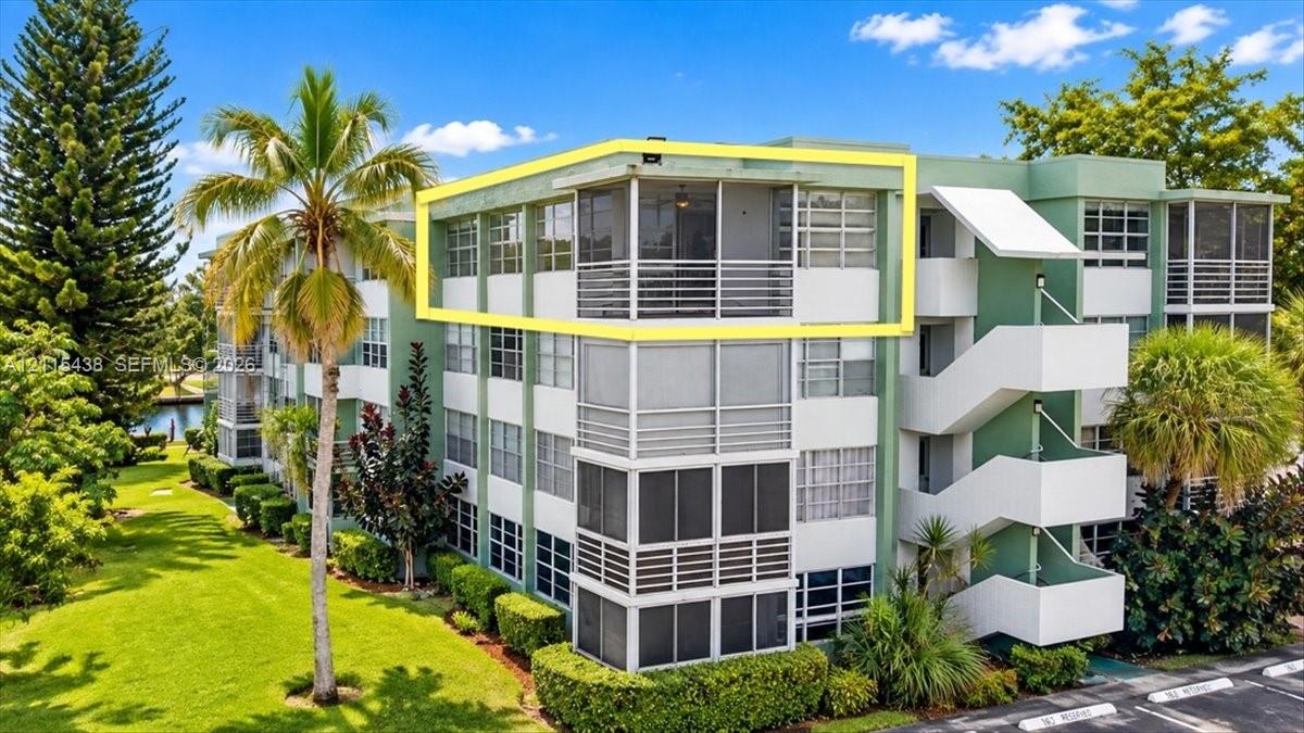 Multi-story residential building featuring a screened balcony with horizontal railing, exterior stairwell, and manicured landscaping