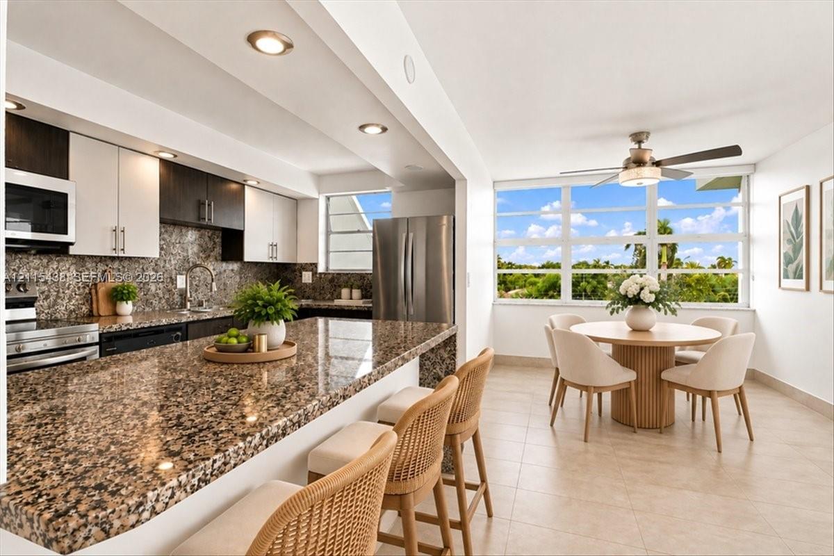 Kitchen featuring stone countertops, two-tone cabinetry, stainless steel appliances, recessed lighting, and large windows with exterior scenery Kitchen featuring stone countertops, two-tone cabinetry, stainless steel appliances, recessed lighting, and large windows with exterior scenery