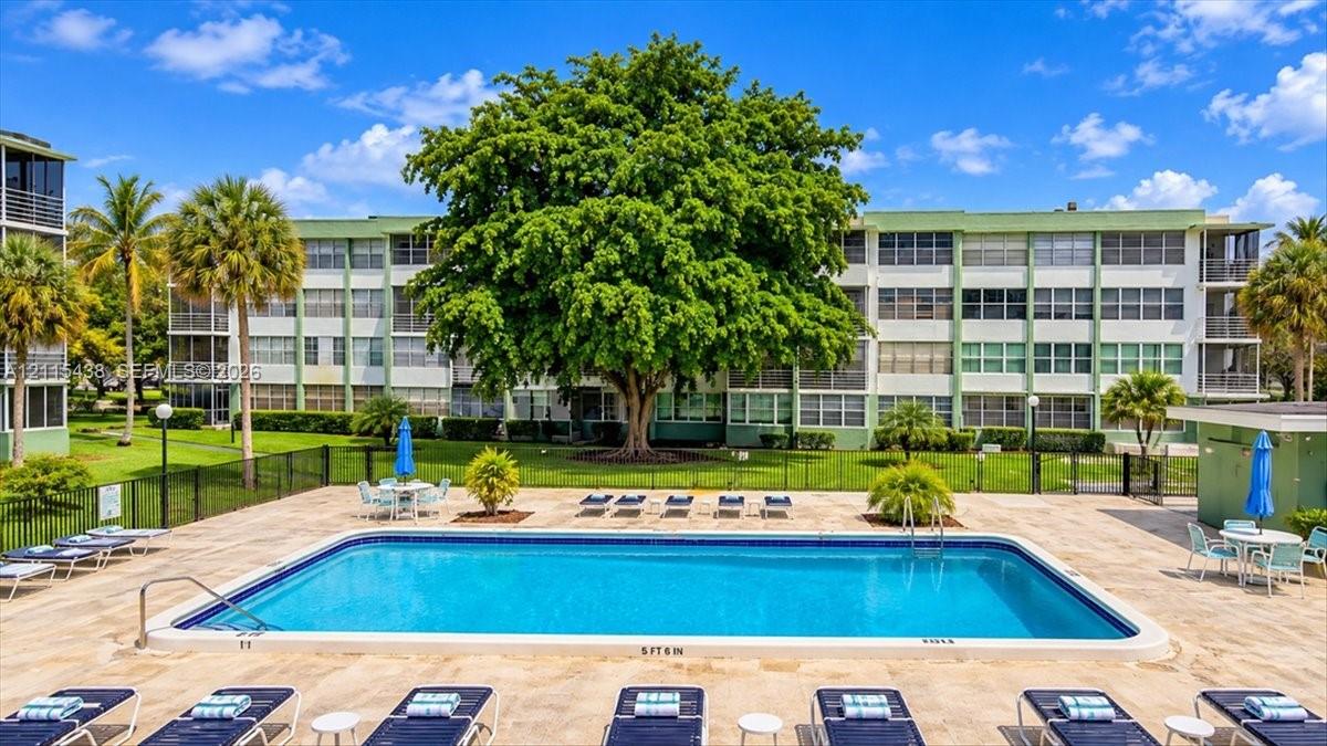Swimming pool featuring a concrete deck, metal perimeter fencing, and mature landscaping