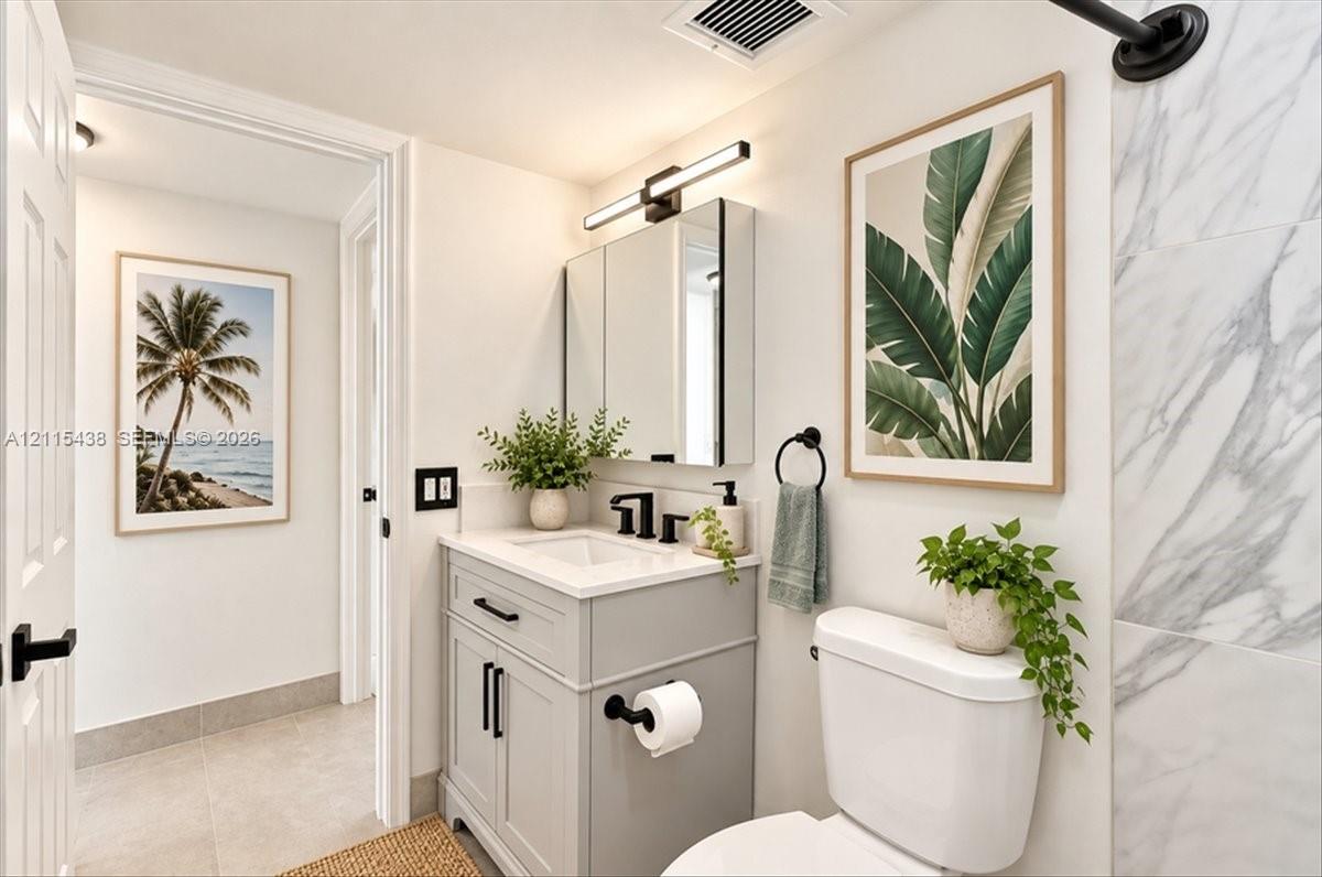Bathroom featuring a vanity with shaker-style cabinetry and matte black hardware, integrated medicine cabinet with linear lighting, stone-finish shower surround, and tile flooring