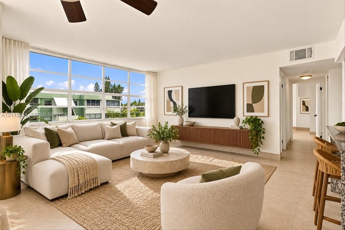Living area featuring expansive floor-to-ceiling windows, neutral tile flooring, a wall-mounted floating wood-finish media console, and an integrated ceiling fan Living area featuring expansive floor-to-ceiling windows, neutral tile flooring, a wall-mounted floating wood-finish media console, and an integrated ceiling fan