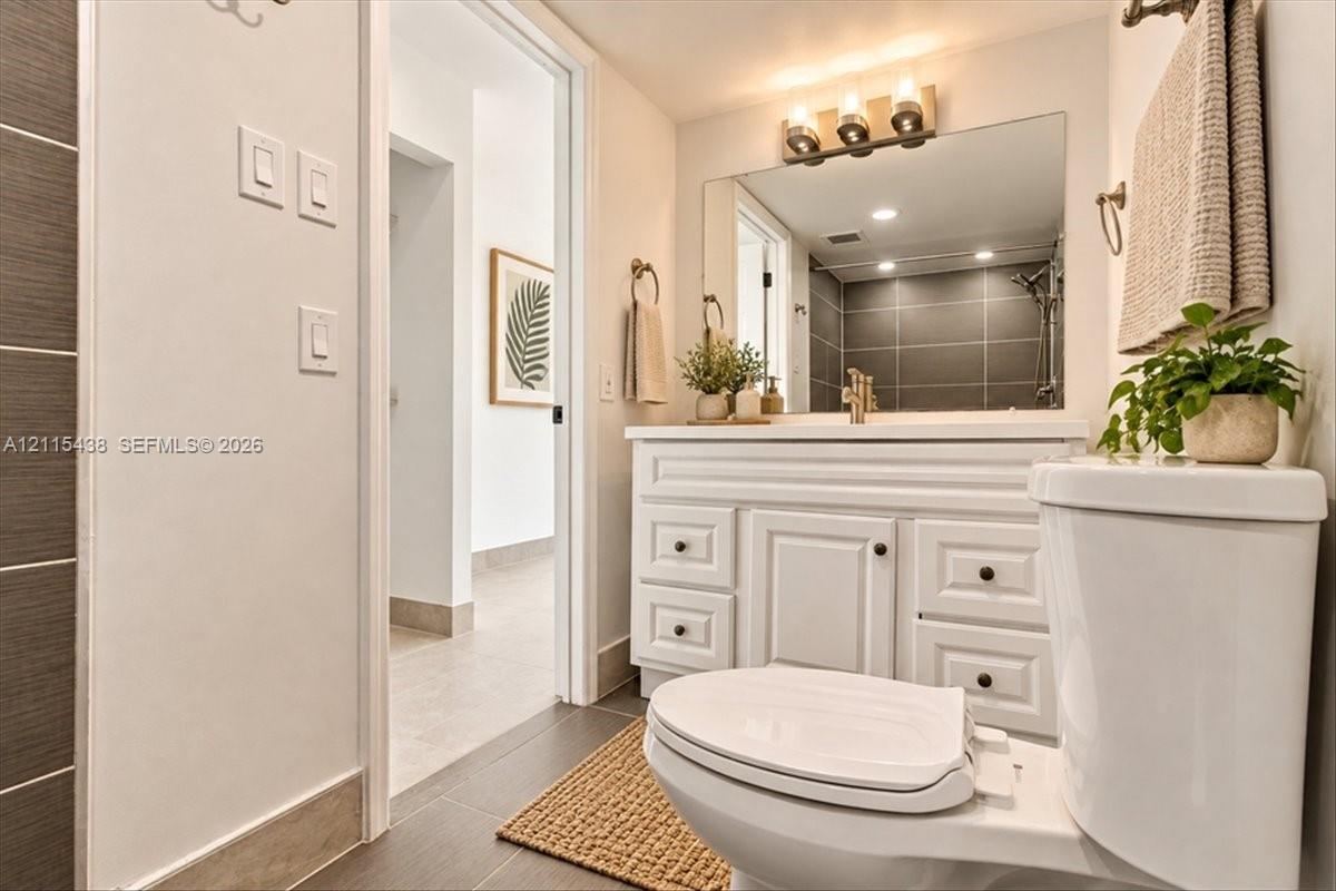 Bathroom featuring a white vanity cabinet with shaker-style drawers, large wall-mounted mirror, three-light fixture, and dark-toned horizontal tile work