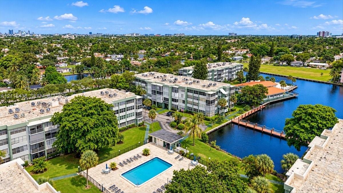 Aerial perspective of a multi-story residential complex featuring a swimming pool with paved deck, canal-side dock, manicured landscaping, and mature palms