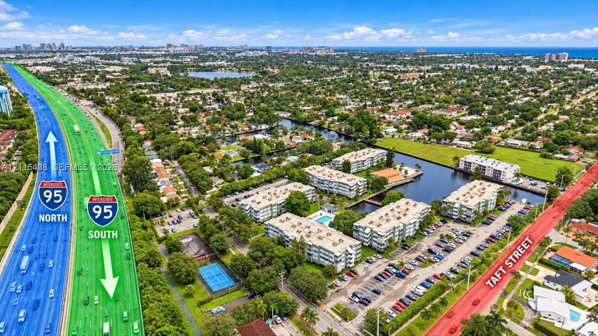 Aerial perspective featuring multi-story residential buildings, water canal frontage, surface parking lots, and an on-site tennis court