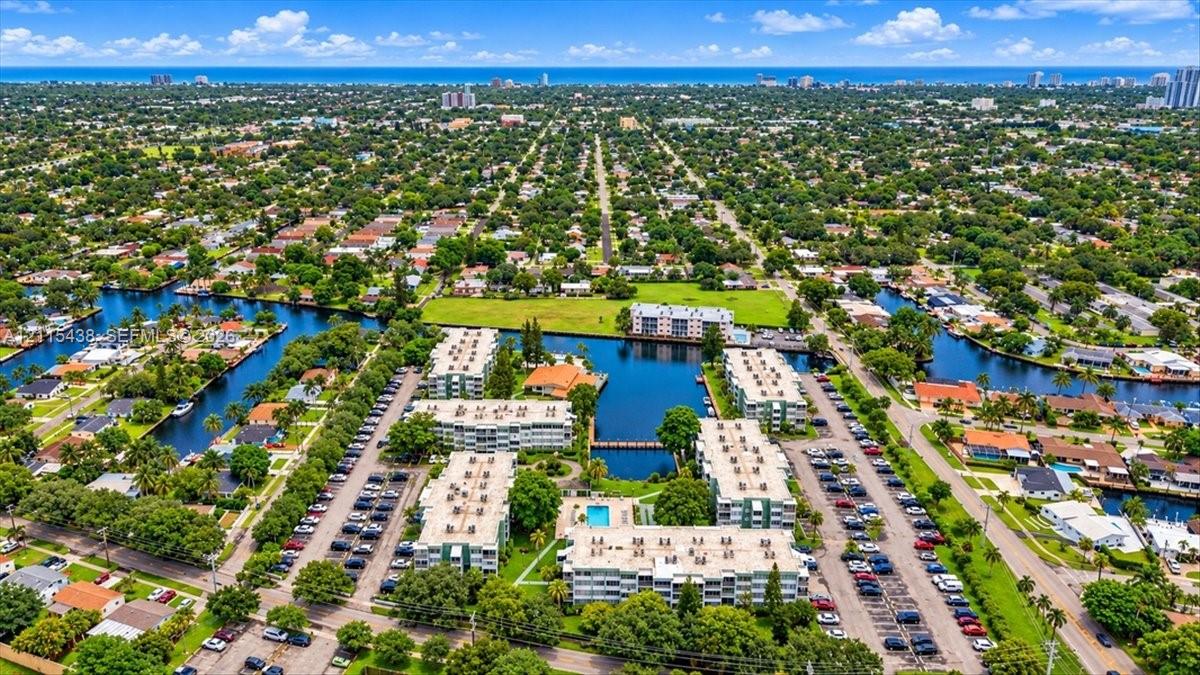 Aerial perspective featuring multi-story residential buildings, a centered swimming pool, canal frontage, paved surface parking, and coastal horizon Aerial perspective featuring multi-story residential buildings, a centered swimming pool, canal frontage, paved surface parking, and coastal horizon