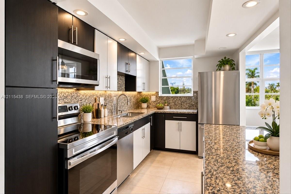 Two-tone cabinetry with contrasting upper and lower finishes, stone countertops, stainless steel appliances, recessed ceiling lighting, and tile flooring Two-tone cabinetry with contrasting upper and lower finishes, stone countertops, stainless steel appliances, recessed ceiling lighting, and tile flooring