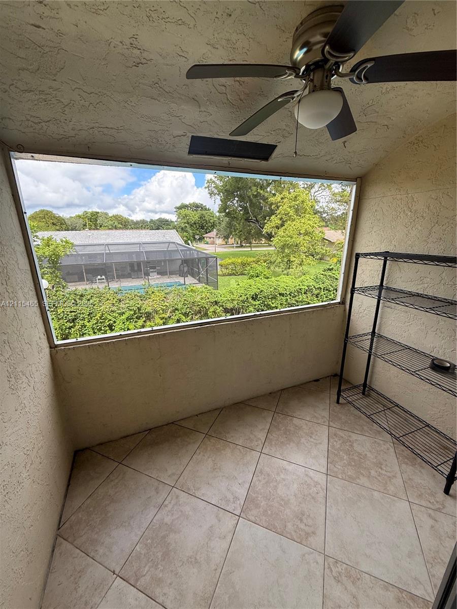 Screened-in balcony featuring neutral tile flooring, stucco wall texture, and a ceiling-mounted fan