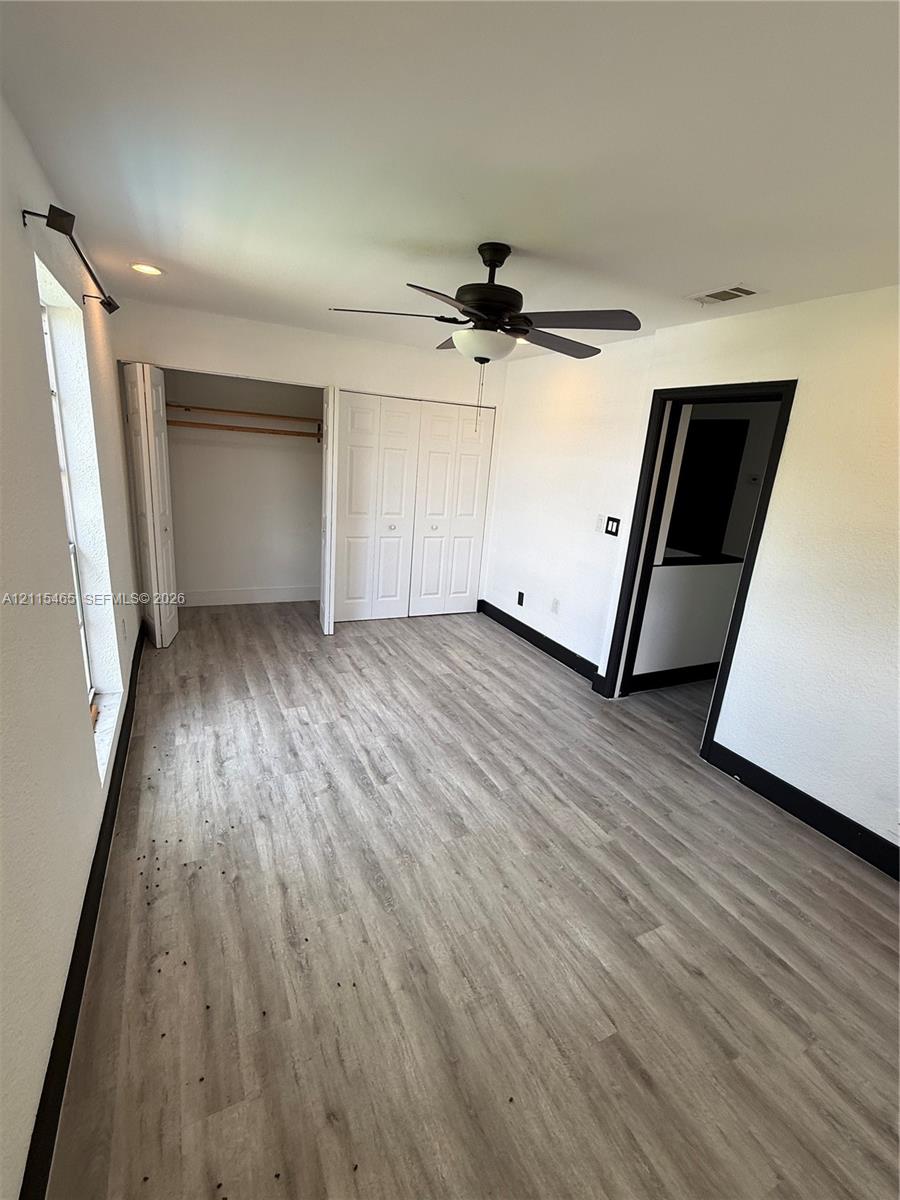 Room featuring wood-finish flooring, a ceiling fan with integrated lighting, bifold closet doors, and contrasting dark trim