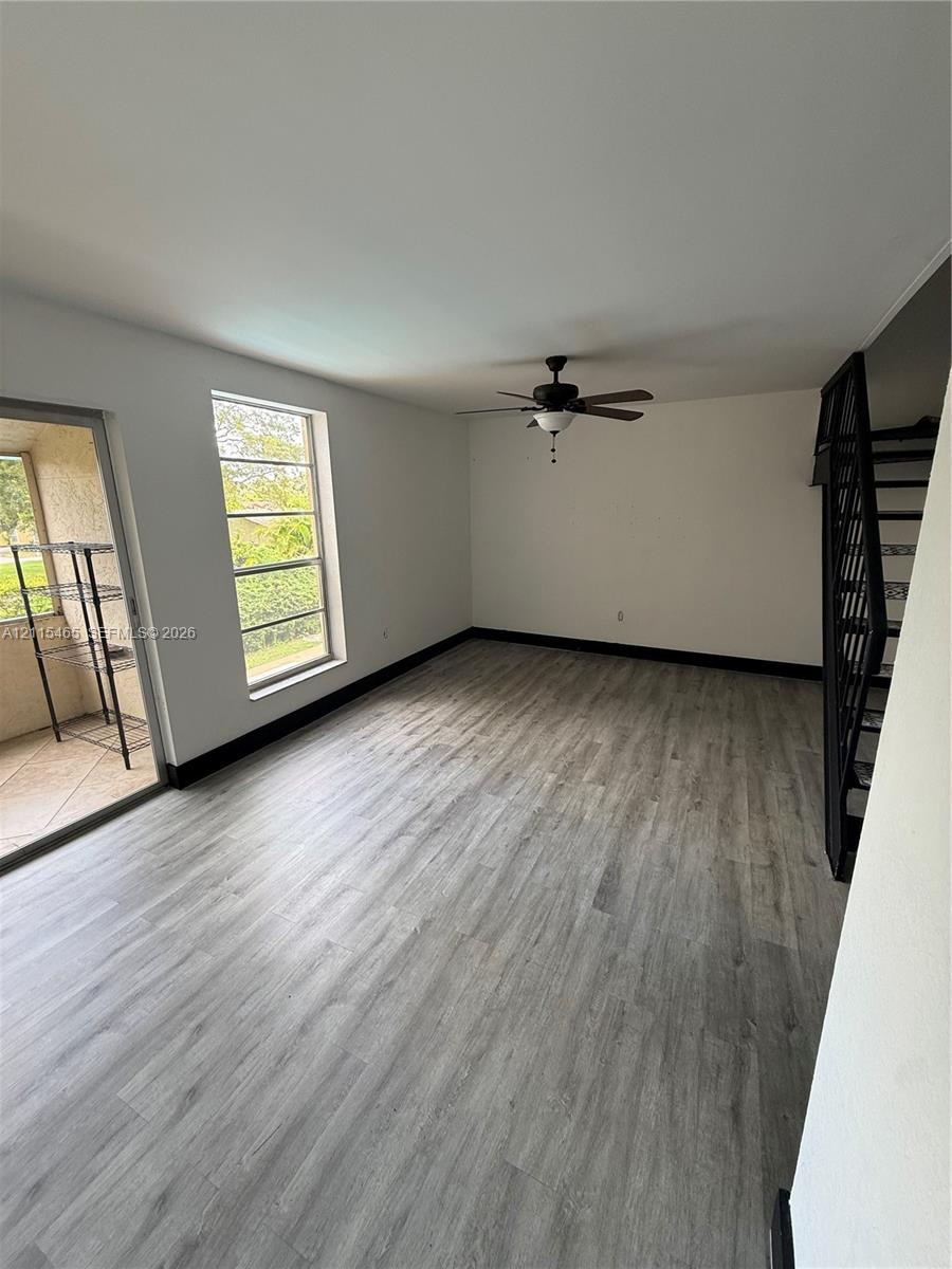 Wood-finish flooring, ceiling fan with integrated light fixture, large window, and metal staircase railing Wood-finish flooring, ceiling fan with integrated light fixture, large window, and metal staircase railing
