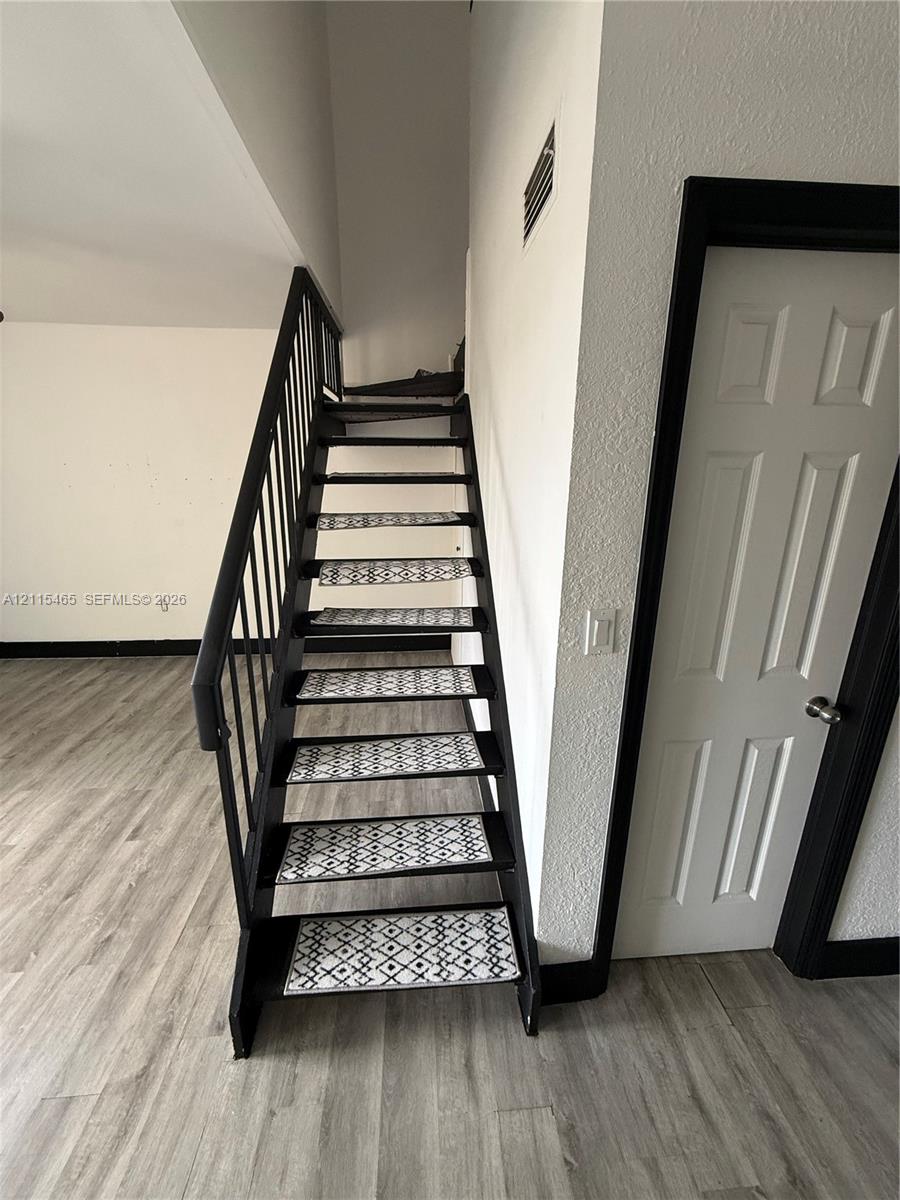 Open-riser staircase featuring a matte black metal frame, geometric patterned tread inserts, and a coordinating metal handrail, complemented by wood-finish flooring Open-riser staircase featuring a matte black metal frame, geometric patterned tread inserts, and a coordinating metal handrail, complemented by wood-finish flooring