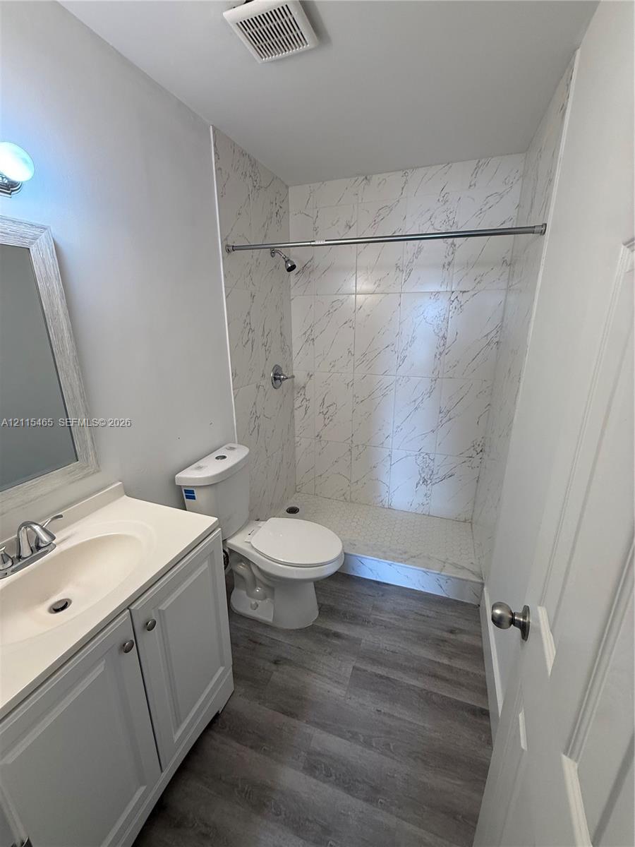 Bathroom featuring a white vanity cabinet, wood-finish flooring, and a walk-in shower enclosure with decorative tile surround