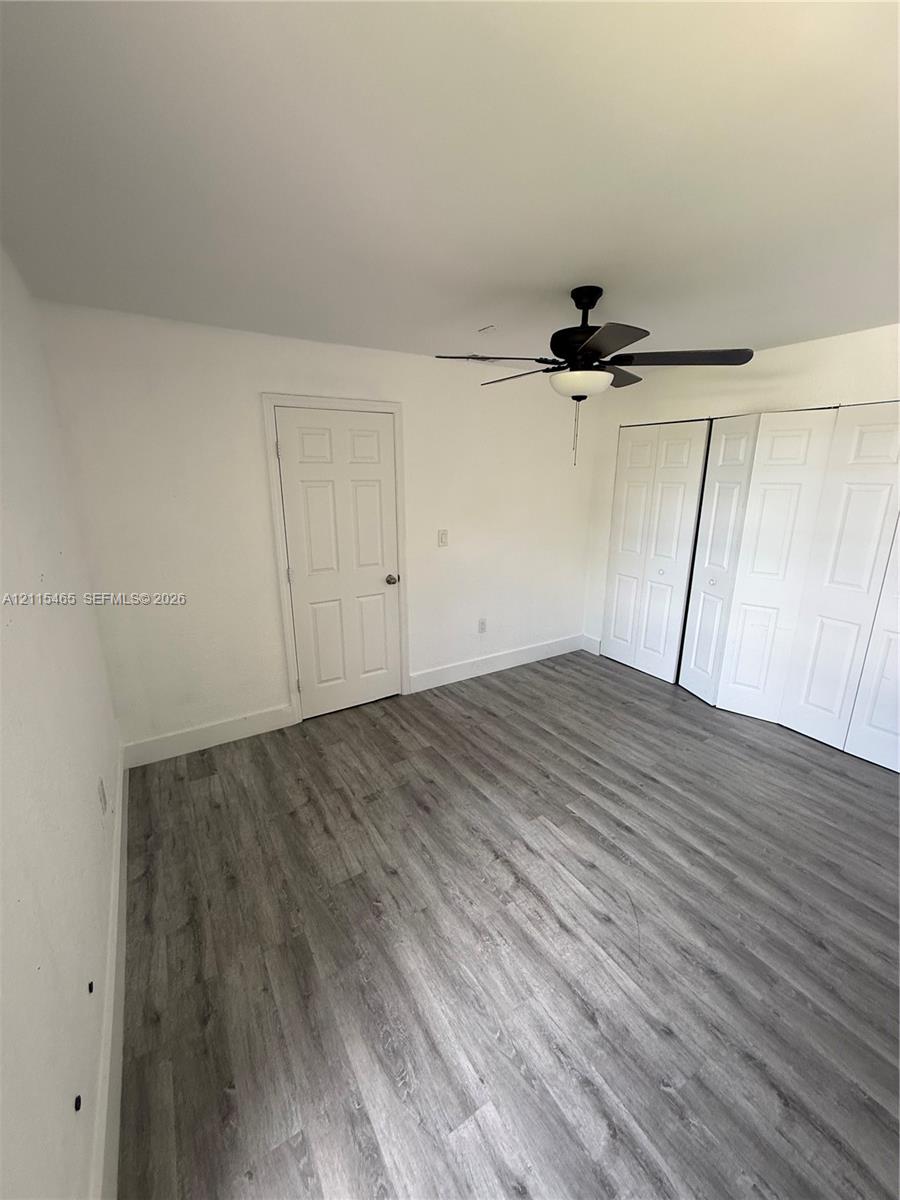 Room featuring wood-finish flooring, a ceiling fan with integrated lighting, a panel door, and dual bi-fold closet doors