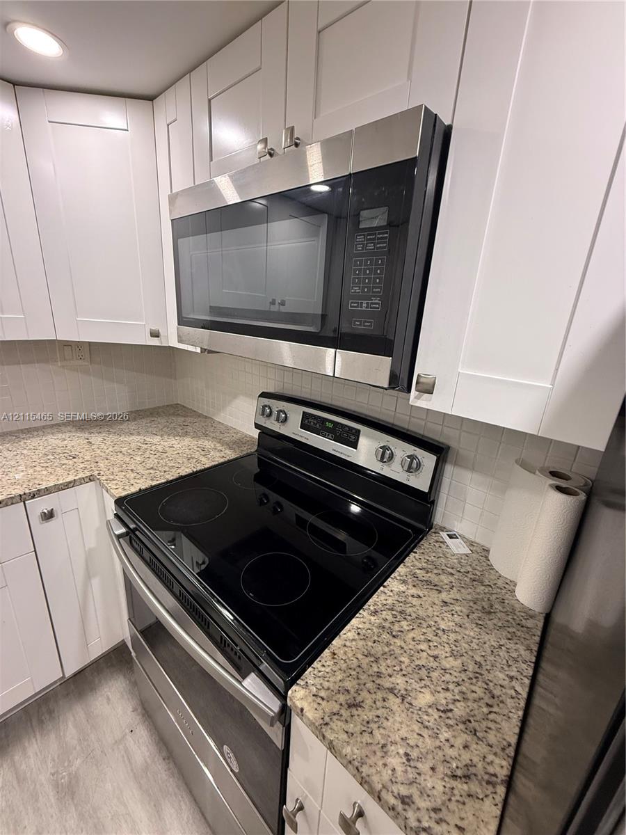 Kitchen featuring white shaker-style cabinetry, speckled stone-finish countertops, stainless steel electric range, over-the-range microwave, and mosaic tile backsplash