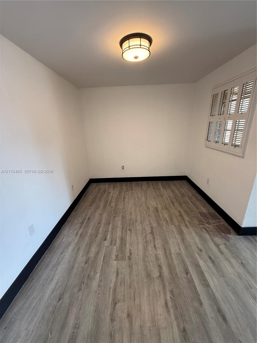 Room featuring wood-finish flooring, high-contrast dark trim, plantation-style window shutters, and a central dome-style flush mount light fixture