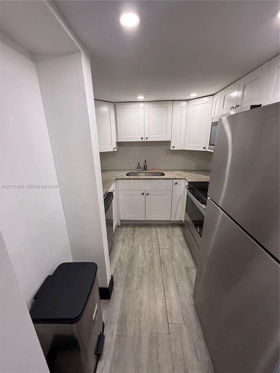 Kitchen featuring white Shaker-style cabinetry, stone-finish countertops, stainless steel appliances, and wood-finish flooring with recessed lighting