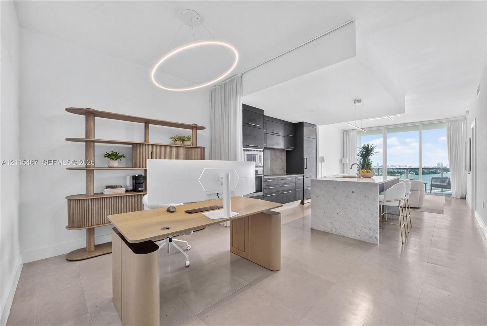 Kitchen featuring dark cabinetry, stone-clad island with waterfall edge, integrated appliances, and large-format tile flooring, accented by a circular LED light fixture