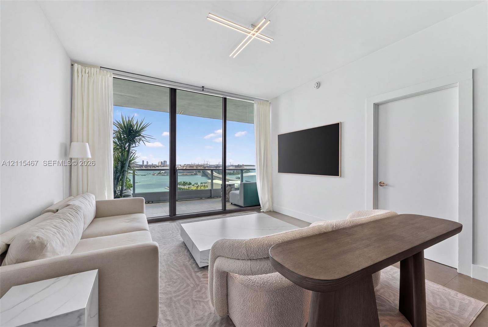 Floor-to-ceiling windows, private balcony, linear geometric ceiling light fixture, and neutral wall-to-wall carpeting