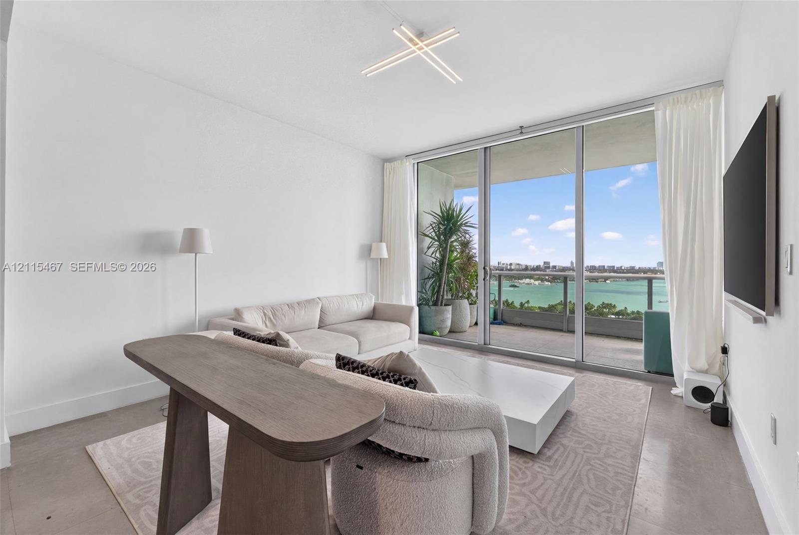 Floor-to-ceiling glass sliding doors, concrete flooring, modern geometric LED ceiling fixture, and covered outdoor balcony