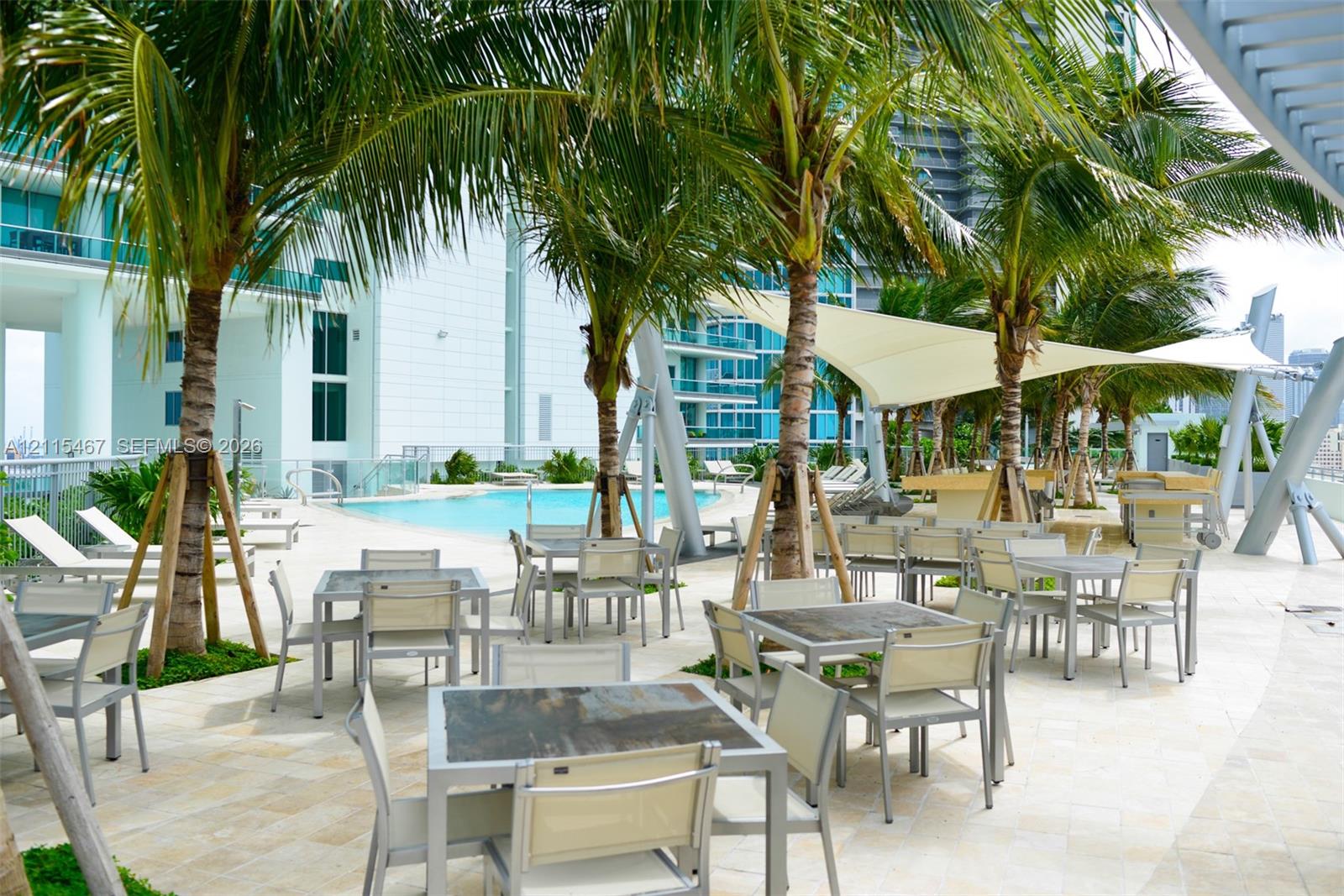 Outdoor terrace featuring natural stone paving, an inground swimming pool, integrated shade structures, and mature palm trees