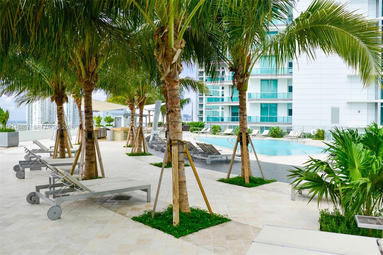 Pool deck featuring stone-tile flooring, mature palm trees, integrated landscaping, and a rectangular swimming pool