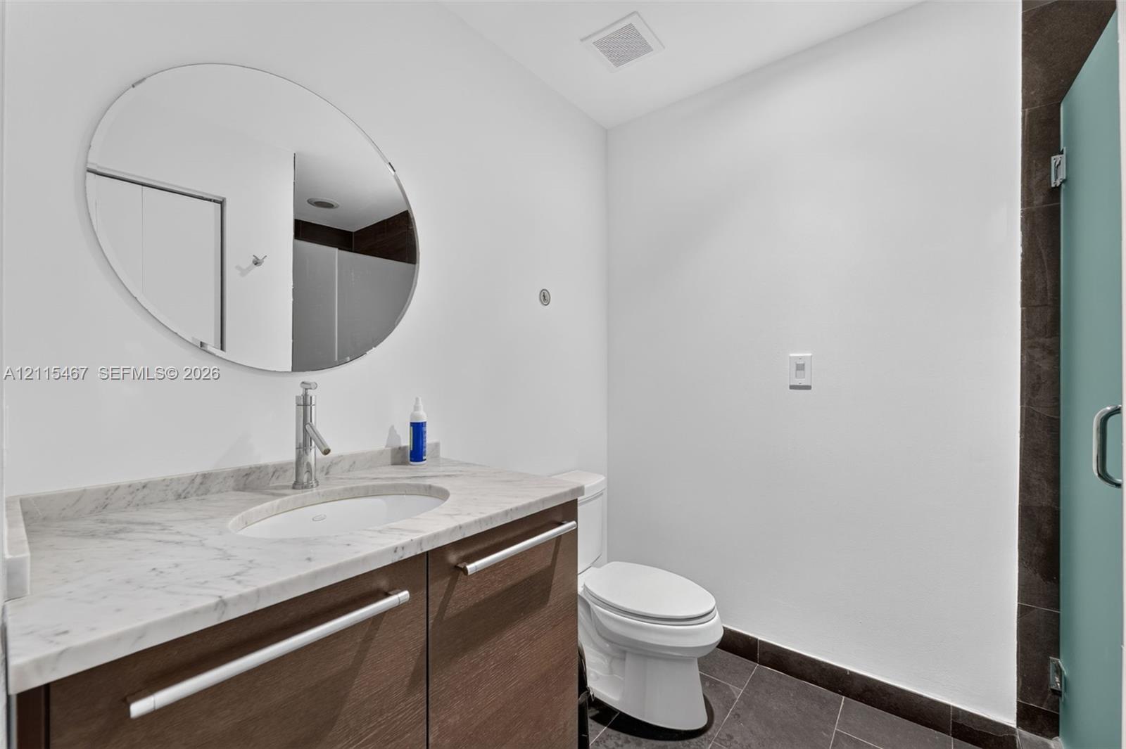 Floating vanity with a stone countertop, oval undermount sink, and polished metal faucet, complemented by a circular wall mirror and dark tile flooring