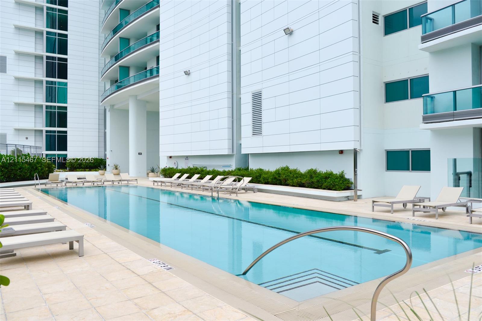 Rectangular lap pool featuring stone-tile decking, integrated entry steps, stainless steel handrails, and surrounding manicured hedging